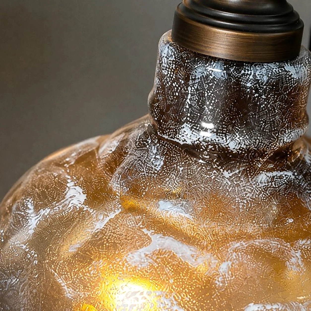 Detailopname van een rokerig grijze, getextureerde glazen lampenkap met een warme amberkleur.