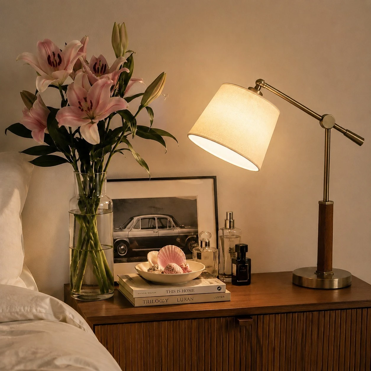 Lampada da tavolo con braccio orientabile in tessuto bianco, accesa accanto a libri e fiori.
