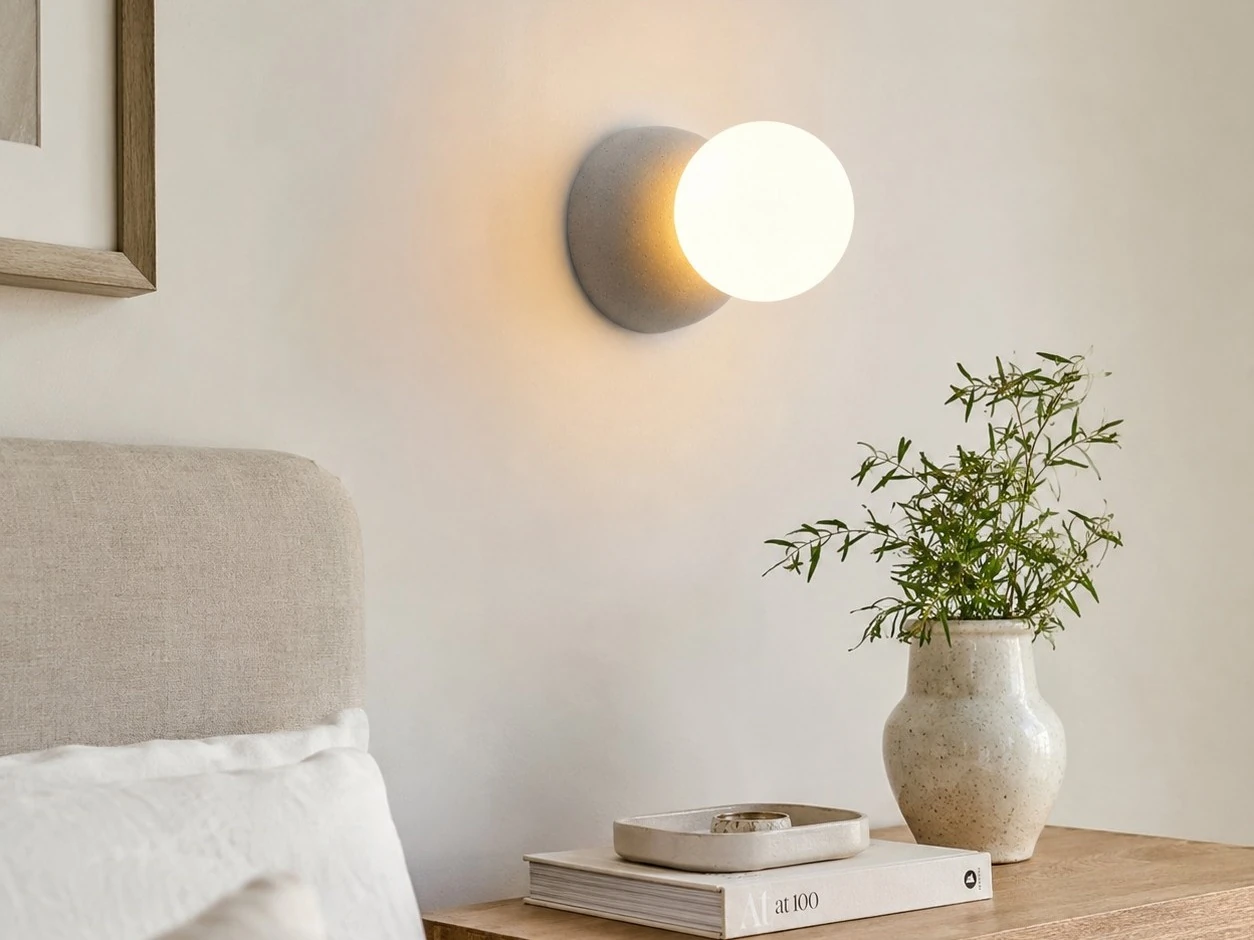 Szara betonowa lampa ścienna z mlecznego szkła zamontowana obok łóżka