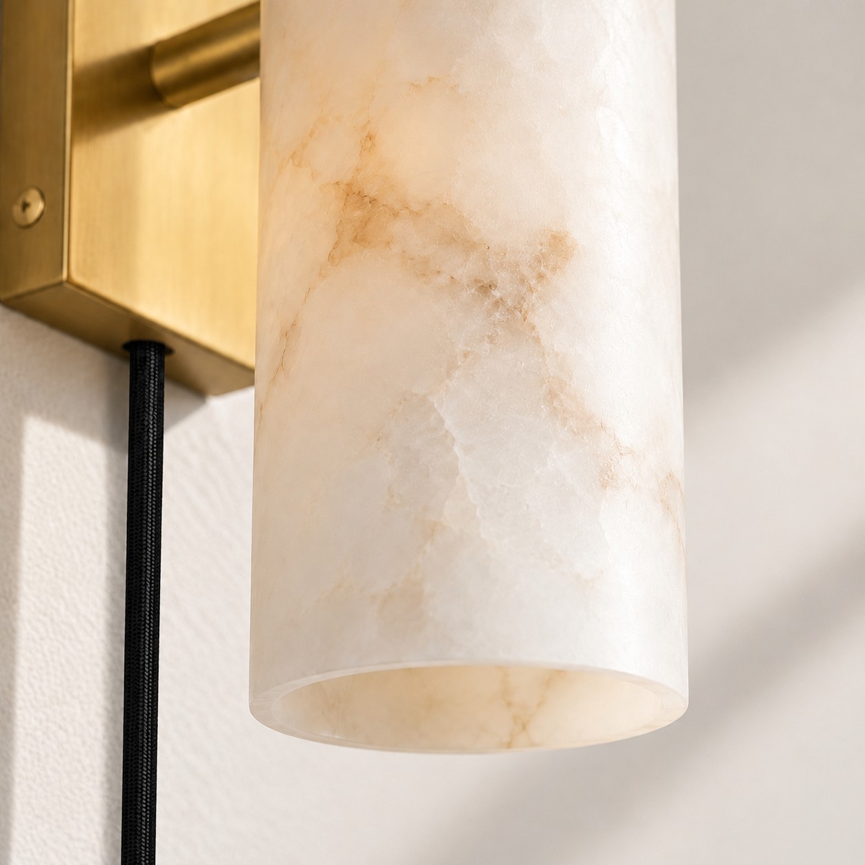 Open end of a veined alabaster tube beside a brass plate and a hanging black cord