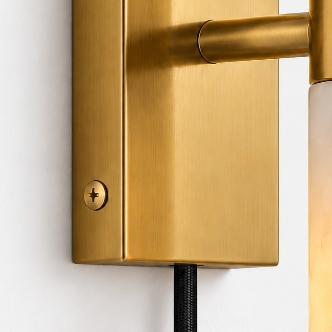 Brushed brass wall plate with a mounting screw and a black cord leaving the bottom edge
