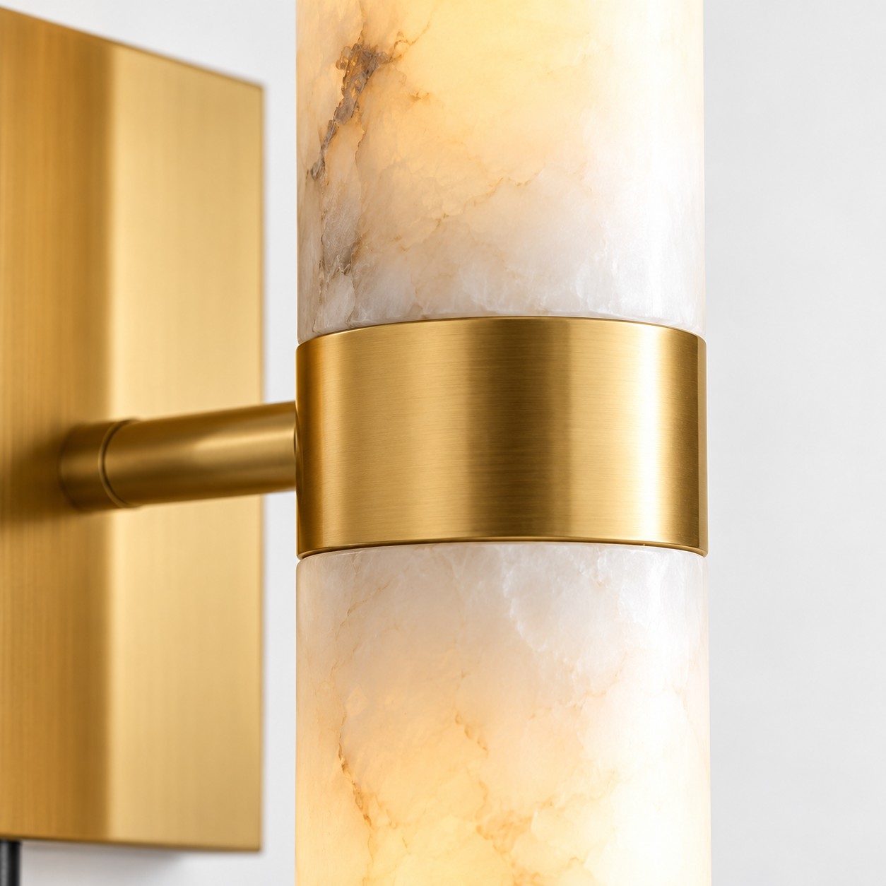 Lit veined alabaster tubes joined by a brushed brass band, with the arm returning to the plate