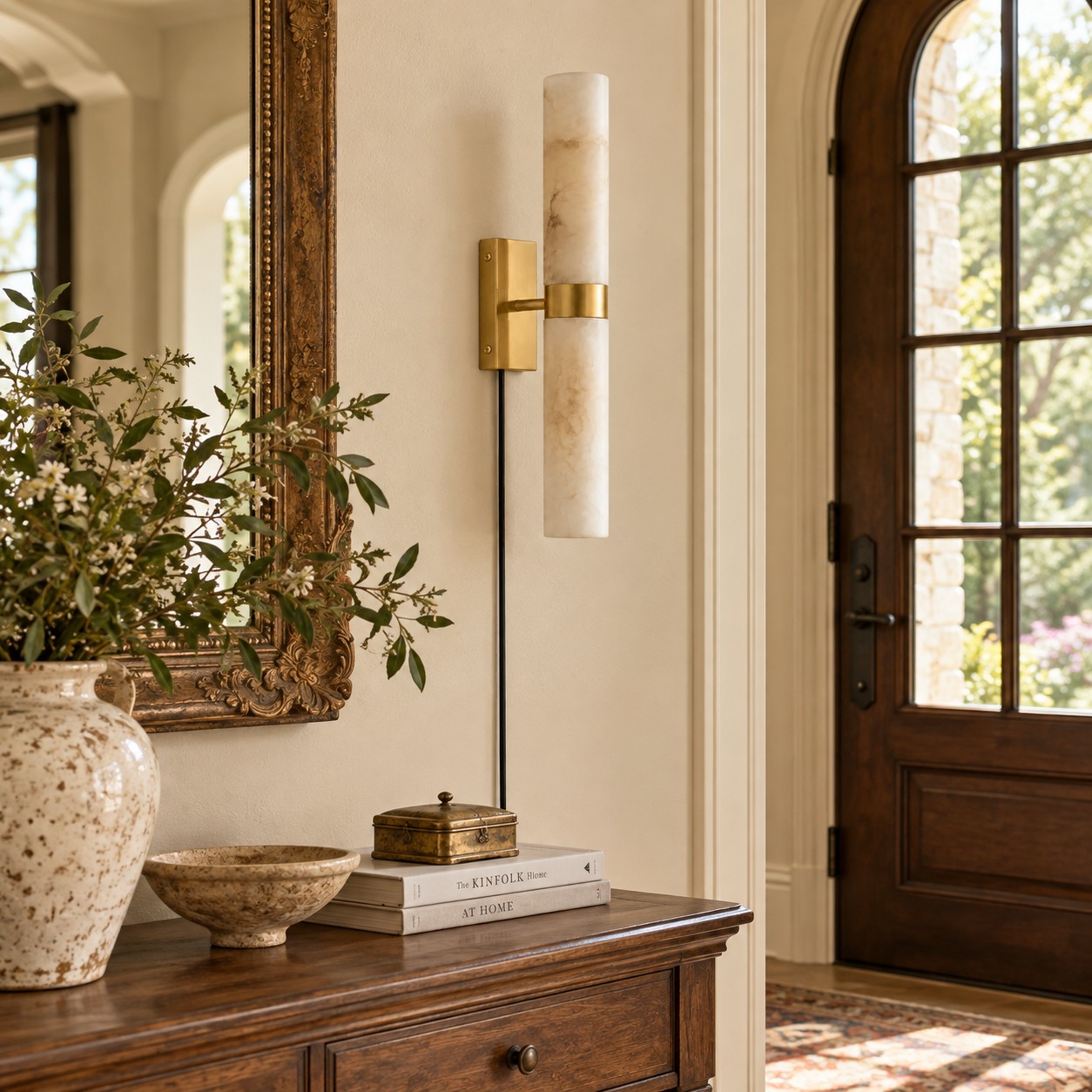 Unlit brass and alabaster sconce beside an ornate mirror, above a wood console in an entry