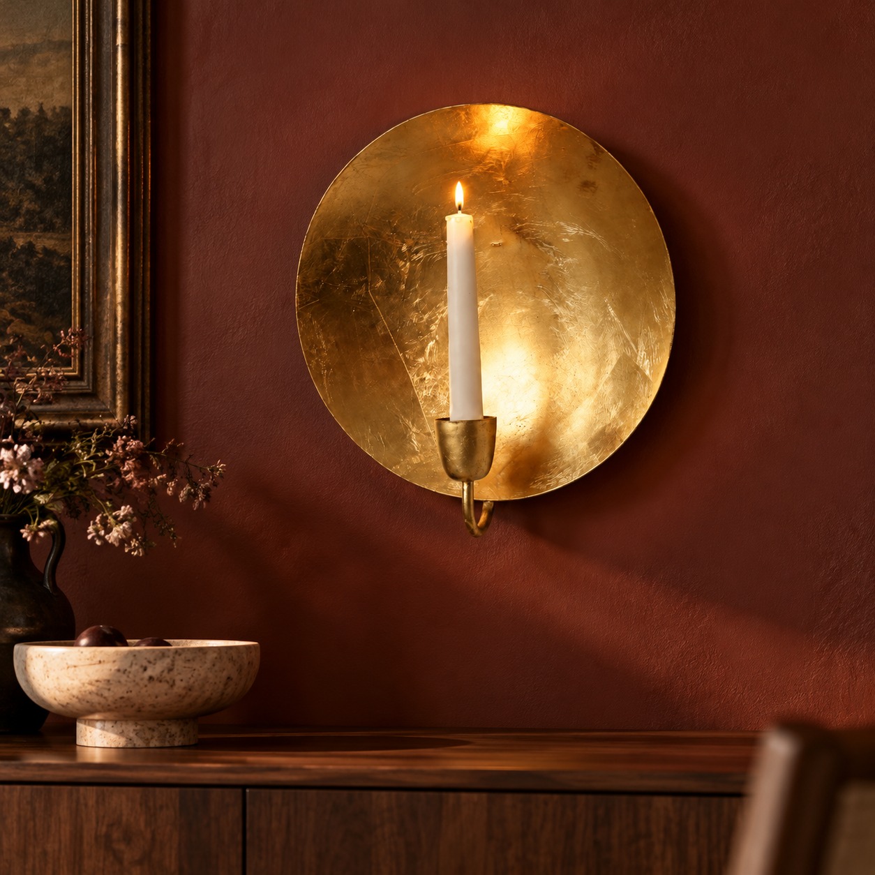 Round gold leaf wall candle holder above a wooden console; illustrative interior