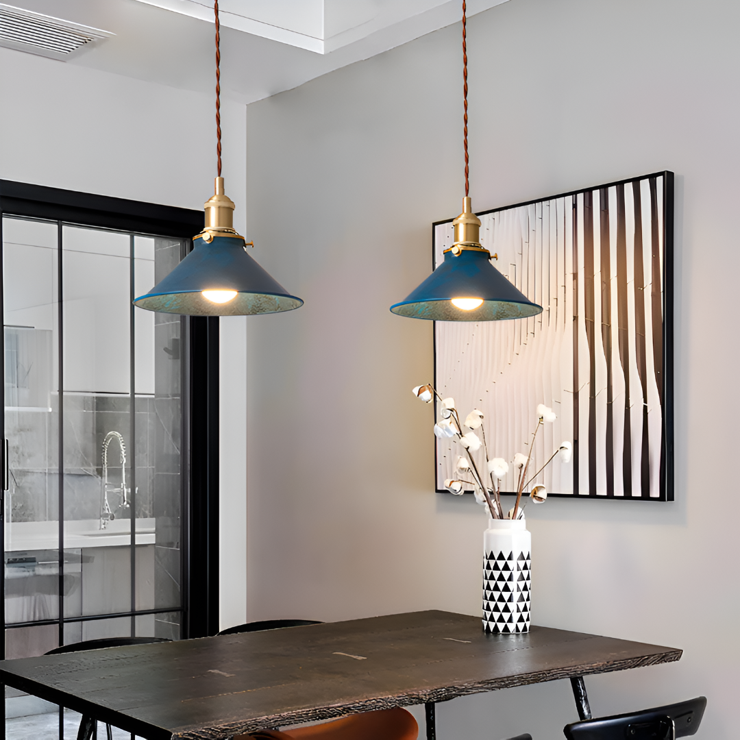 Interior moderno com luminárias pendentes azuis, um vaso com galhos decorativos e uma pintura abstrata emoldurada.