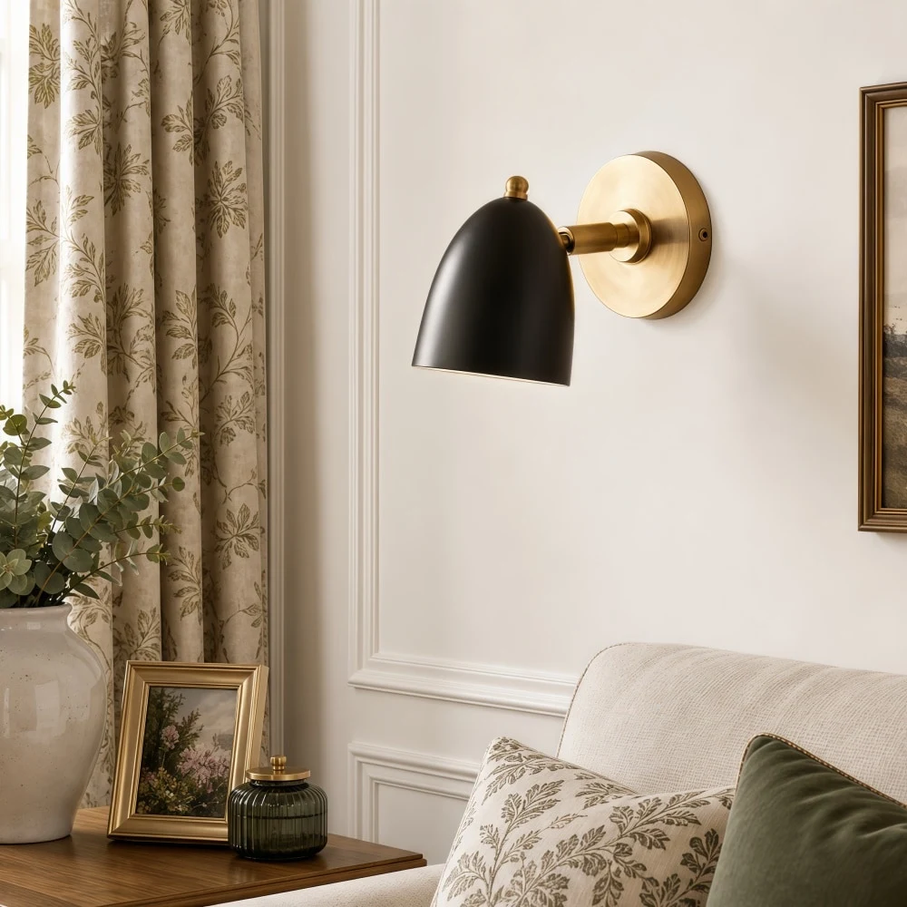 Svart och guldfärgad vägglampa ovanför ett elegant sänghörn