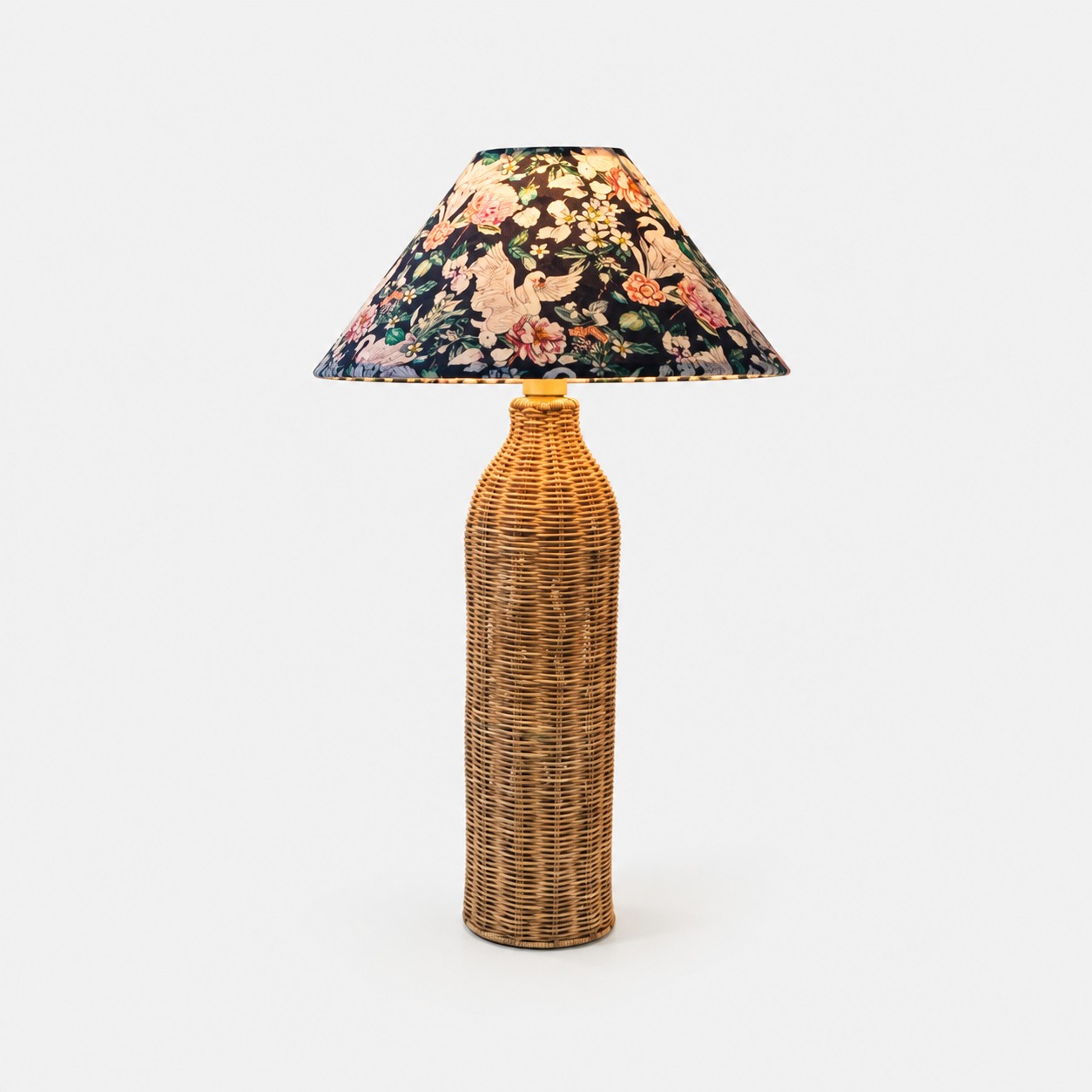 Lampada da tavolo in rattan intrecciato con paralume in tessuto con motivi botanici a forma di uccelli.