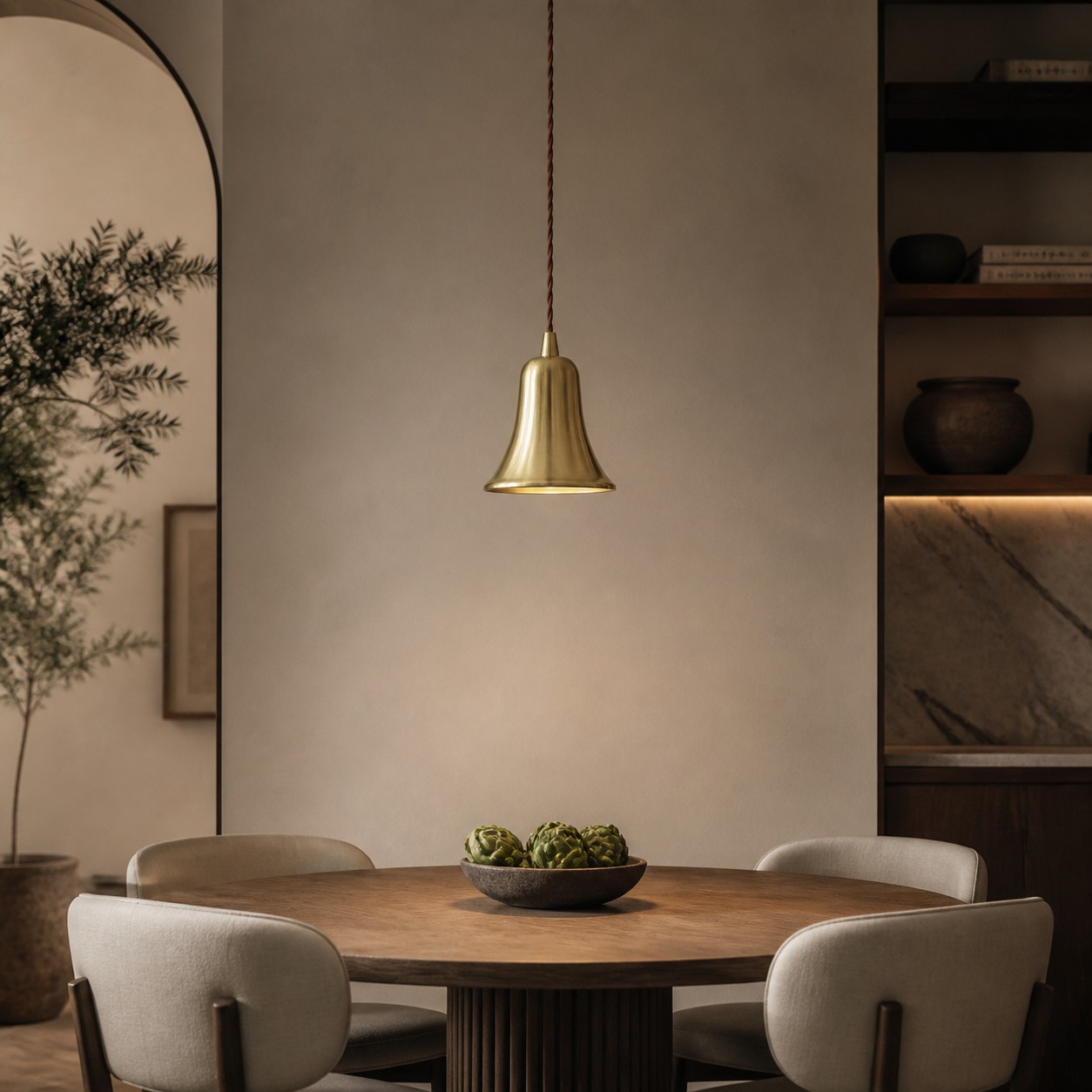 Lámpara colgante de latón natural en forma de campana sobre una cálida mesa de comedor.